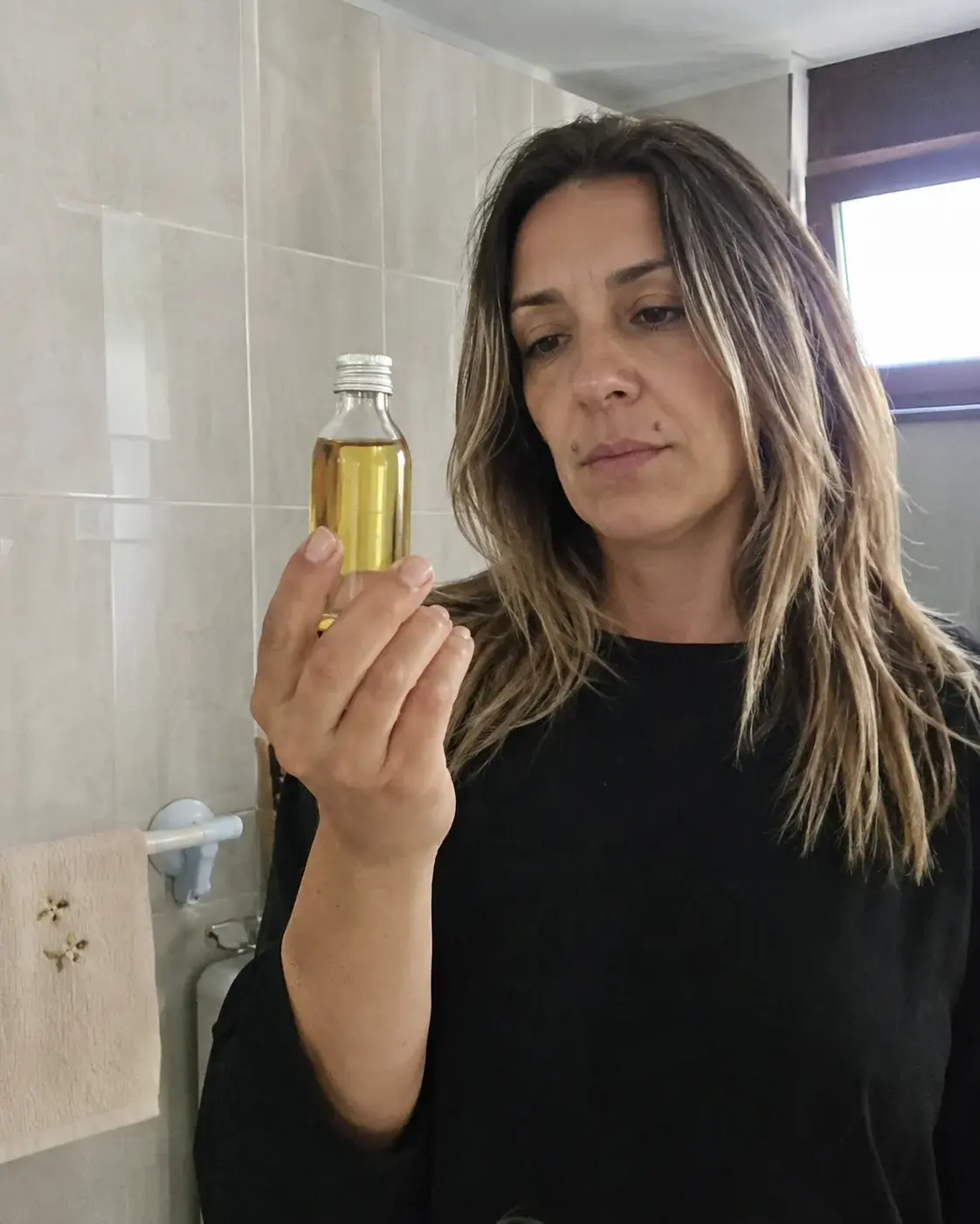 Žena sa balayaž kosom drži flašicu ricinusovog ulja