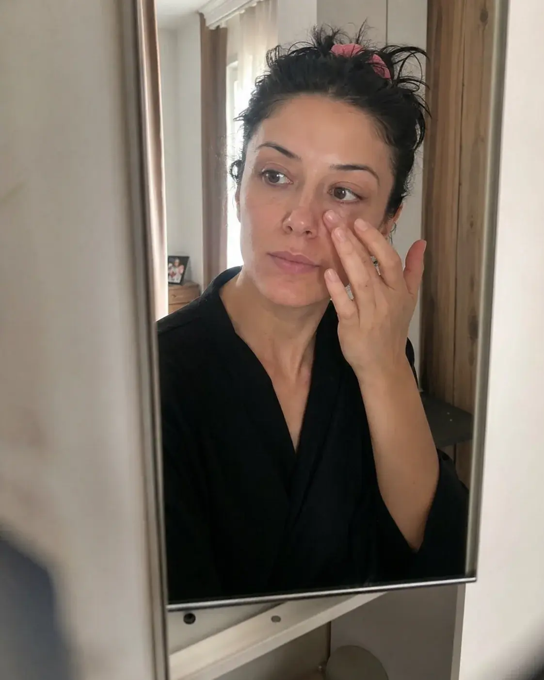 Žena nanosi ricinusovo ulje ispod očiju pred ogledalom ujutro