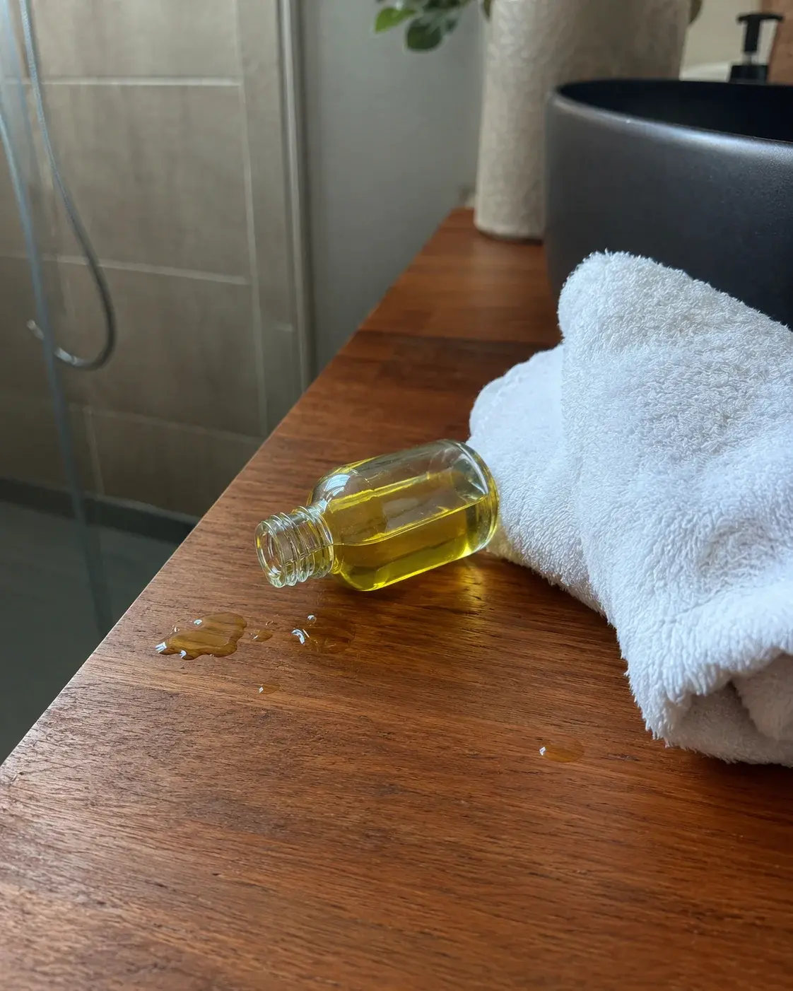 Prevrnuta bočica ricinusovog ulja sa prosutim kapljicama na drvenom pultu