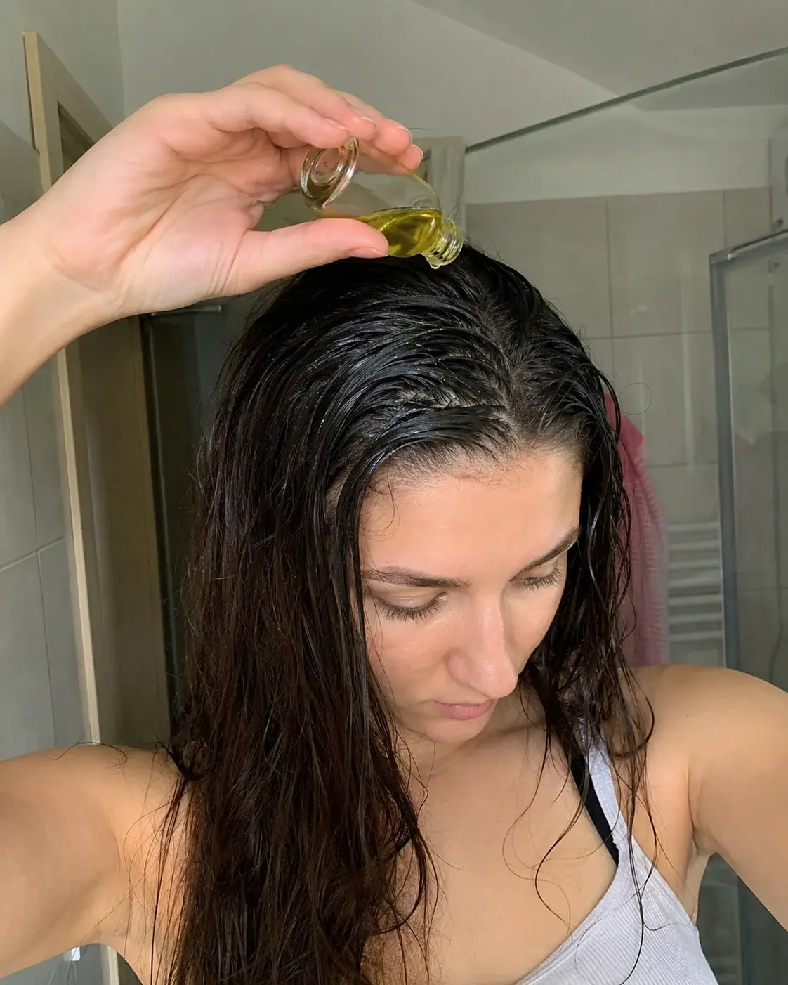 Žena nanosi ricinusovo ulje na masnu kosu pre pranja u kupatilu