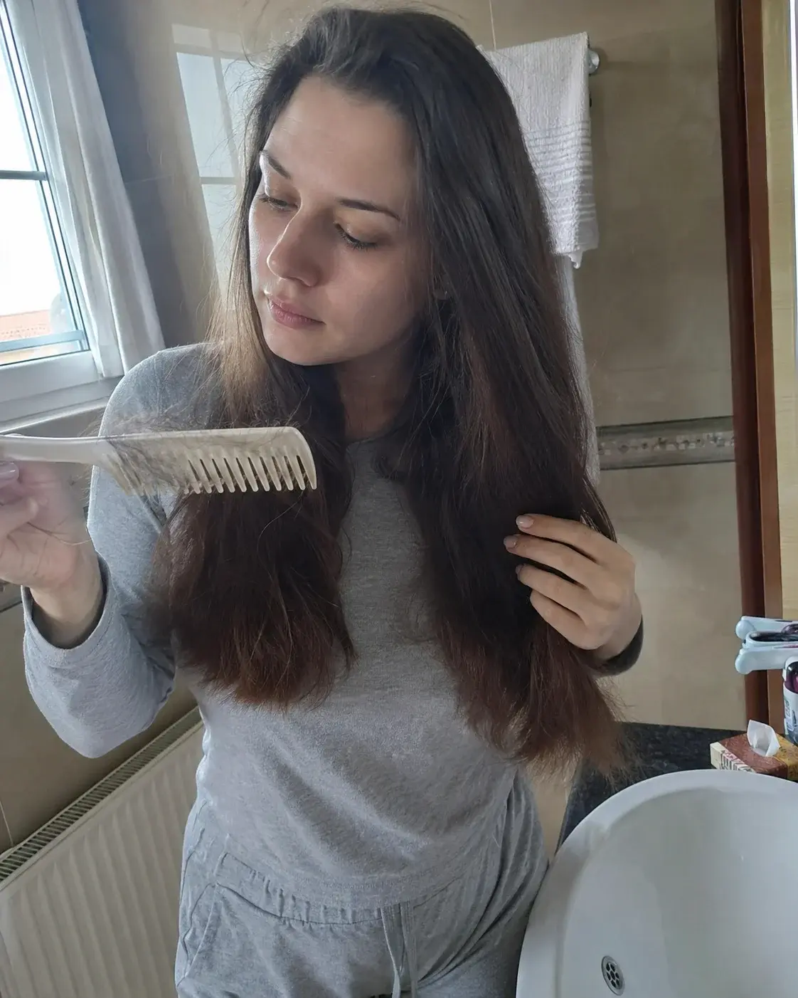 Mlada majka češlja kosu pred kupatilskim ogledalom
